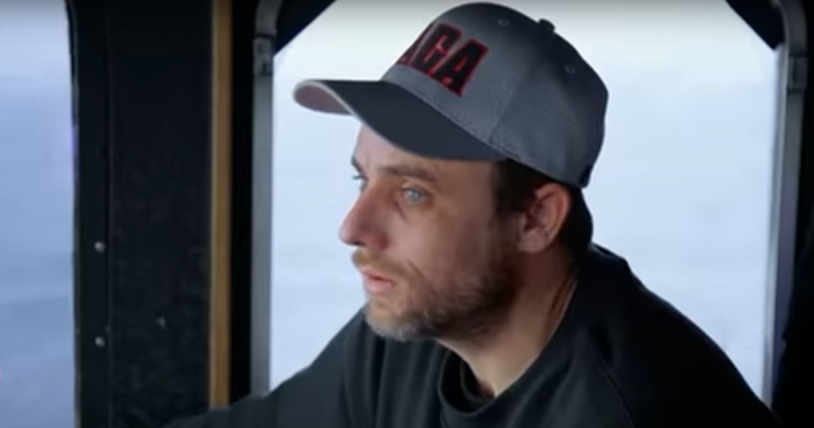 Jake Anderson from right camera angle wears grey hat with lettering, sea in background.