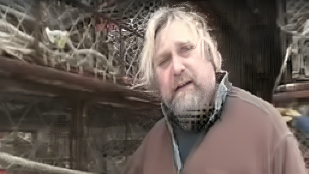 Larry Hendricks wears brown top with collar up, with netting seen behind him.