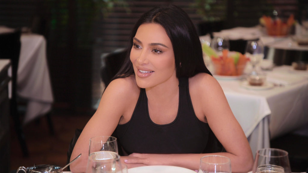 Kim Kardashian smiles with arms folded looking out of shot