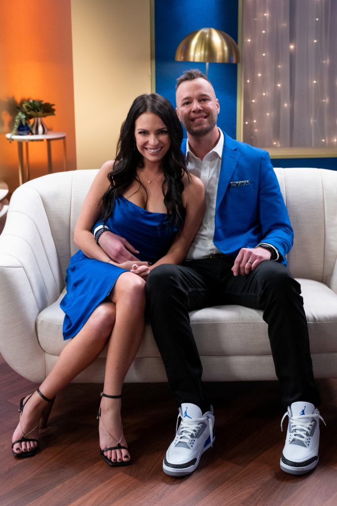 Danielle Ruhl and Nick Thompson hug and smile while wearing blue, sitting on cream sofa, on Love is Blind.