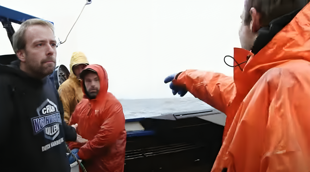 Captain Edgar Hansen looks seriously at Jake Anderson, pictured from behind wearing orange jacket and pointing finger at Matt Bradley, who wears hood up and looks at him on The Northwestern, on Deadliest Catch.