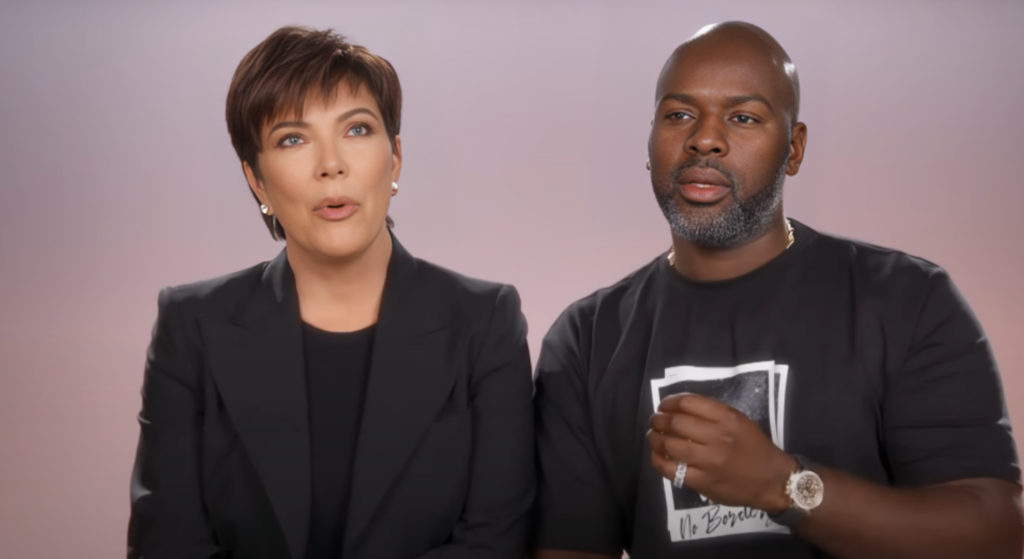 Kris Jenner e Corey Gamble estão ambos vestidos de preto. Ambos parecem surpresos.