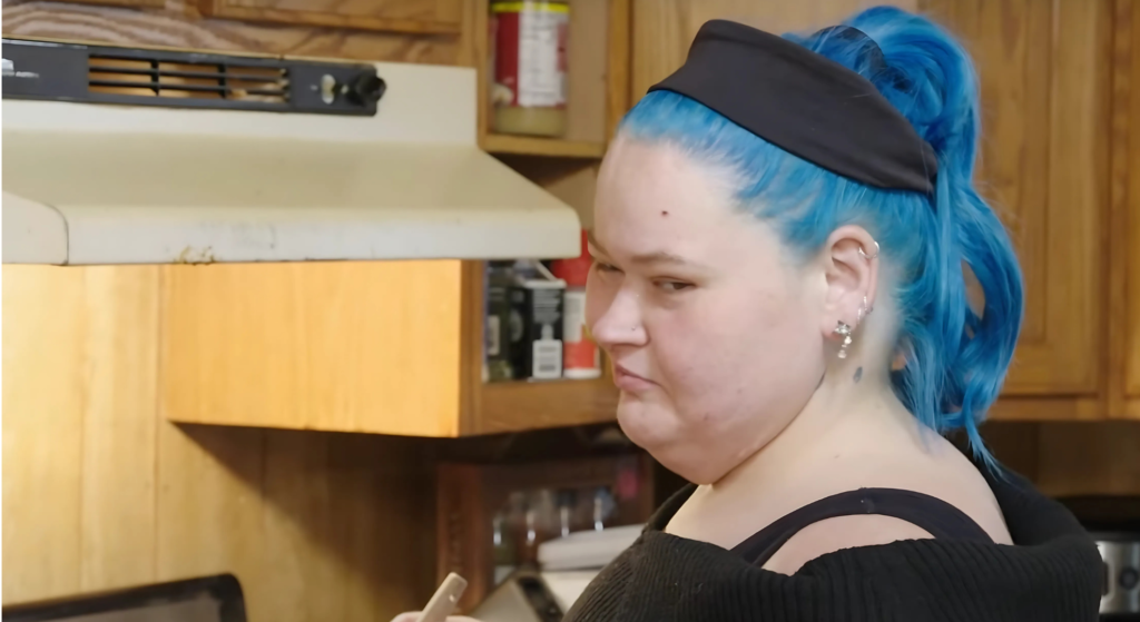 1000-Lb Sisters Amy Slaton cooks food in kitchen looking across camera in front of cooker hood