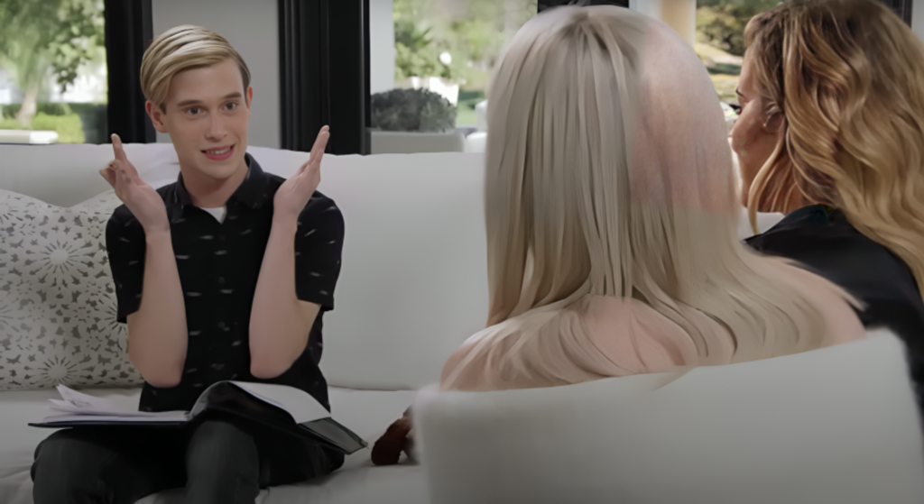 Medium Tyler Henry sits on a couch and throws his hands in the air in shock, the back of Kylie Jenner;s head is visible as she looks at him.