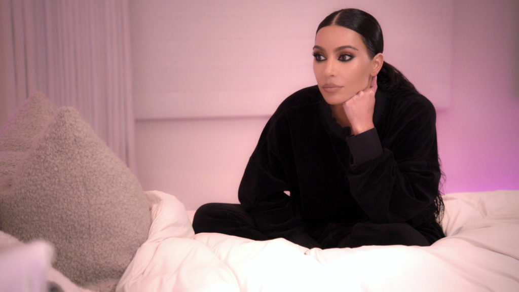 Kim Kardashian sits wearing black outfit looking into distance filming The Kardashians