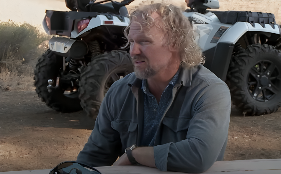 Kody Brown leans arm on table facing left with quad bike behind on Sister Wives.