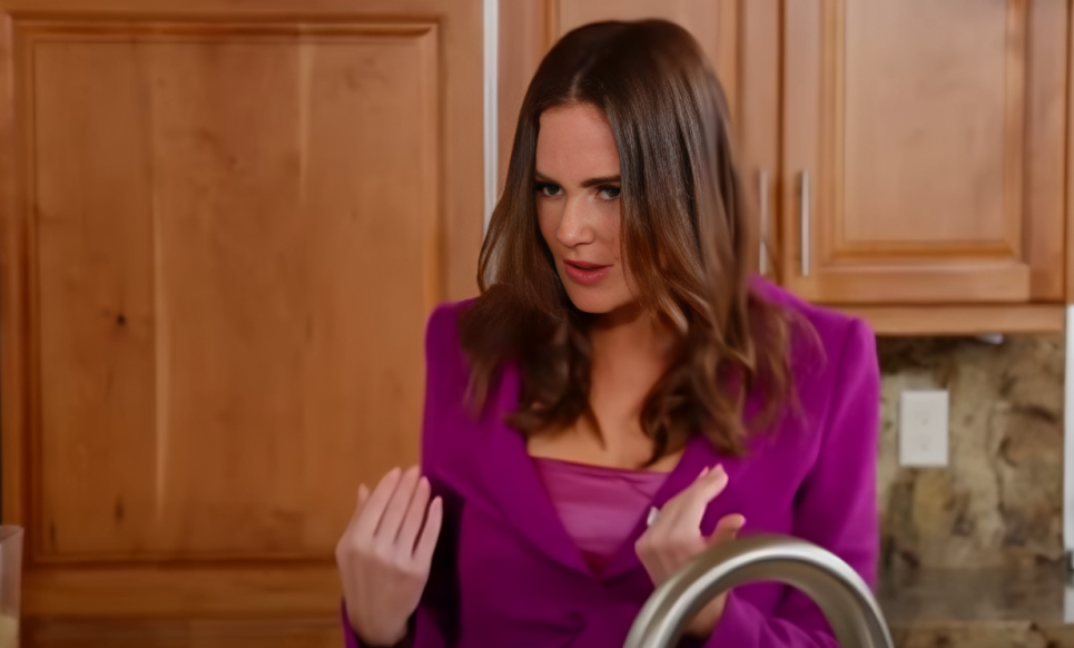 Meredith Marks wears purple blazer as she stands in wood kitchen, pointing hands at herself, on RHOSLC.