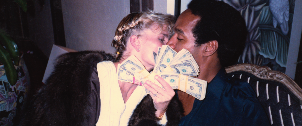 Nicole Brown Simpson holds up wad of money while kissing OJ Simpson.