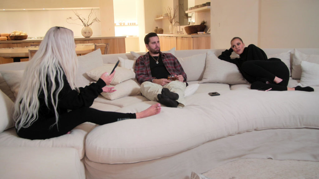 Scott Disick sits on cream sofa with Kim and Khloe Kardashian.