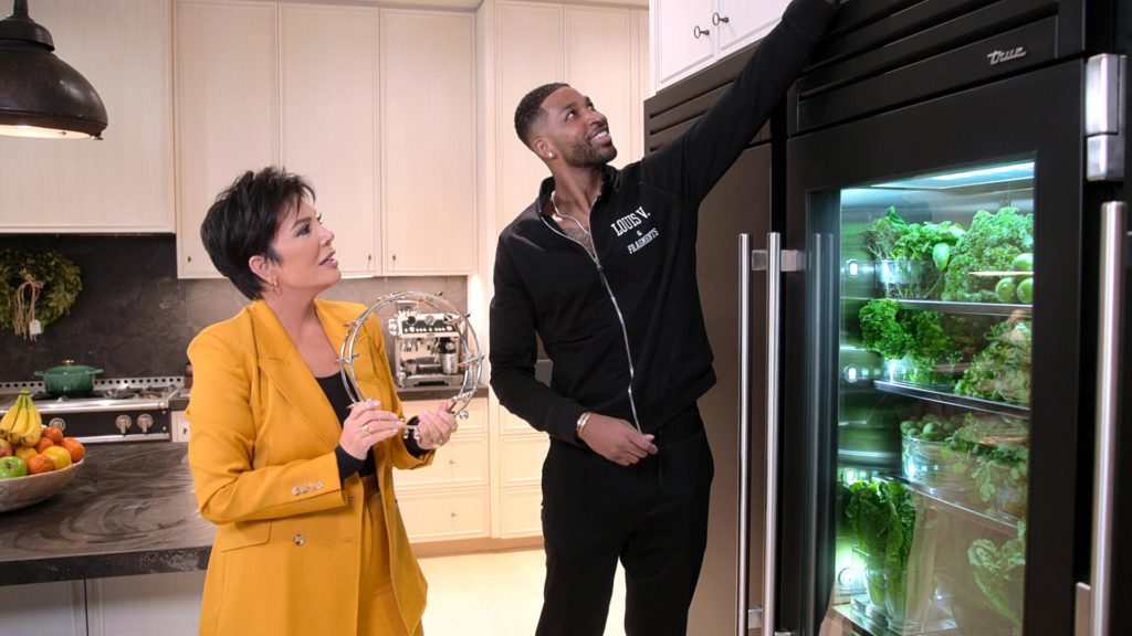 Tristan Thompson reaches for item in kitchen smiling, to right of Kris Jenner, on The Kardashians.