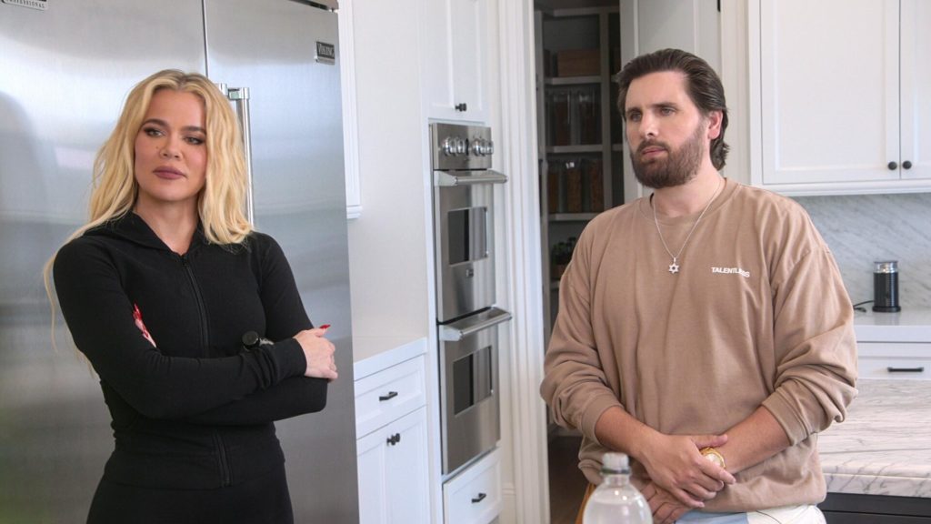 Khloe Kardashian crosses arms and looks to left while Scott Disick stands to her right in kitchen on The Kardashians.